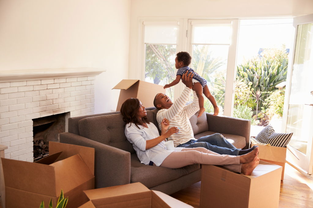 Parents Take A Break On Sofa With Son On Moving Day, father holding son in raised hands